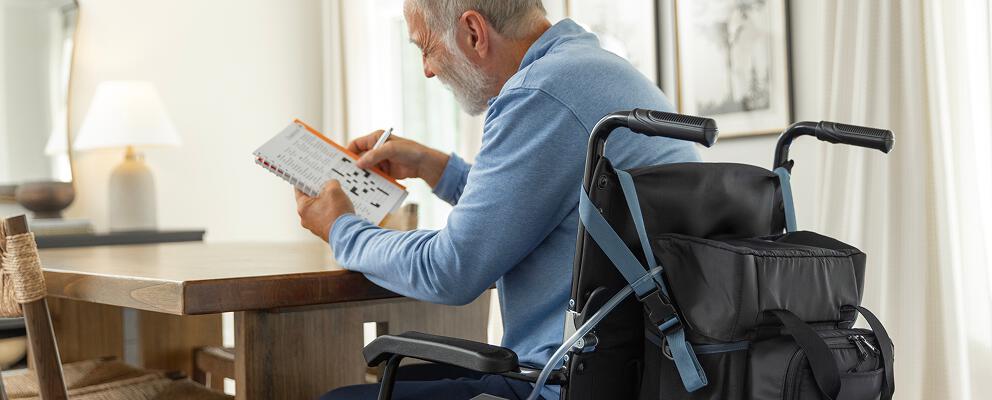 Man doing crossword puzzle in wheelchair with PureWickTM Portable Collection System attached