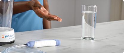 Nurse gestures towards counter with full glass of water, PureWick System, and PureWick Flex