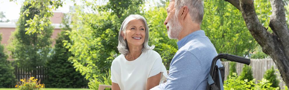 Woman and man in wheelchair with PureWick™ Portable Collection System attached sitting outside and smiling