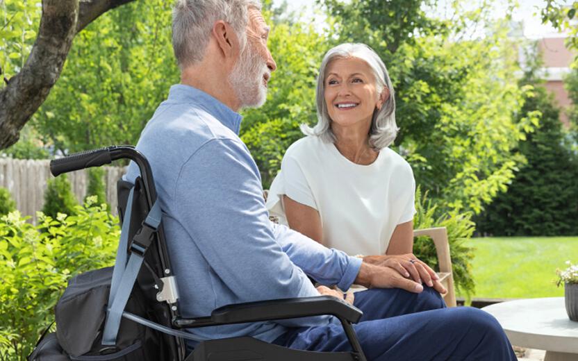Man in wheelchair with PureWick Portable Collection System on back smiling at woman on patio