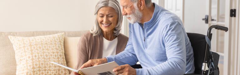 Man in wheelchair and woman smiling and looking at photo album together.