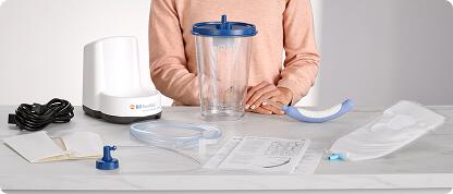 Person stands behind counter with PureWick System Starter Set components, including canister, base, wicks, tubing, cord, privacy cover, and user guide