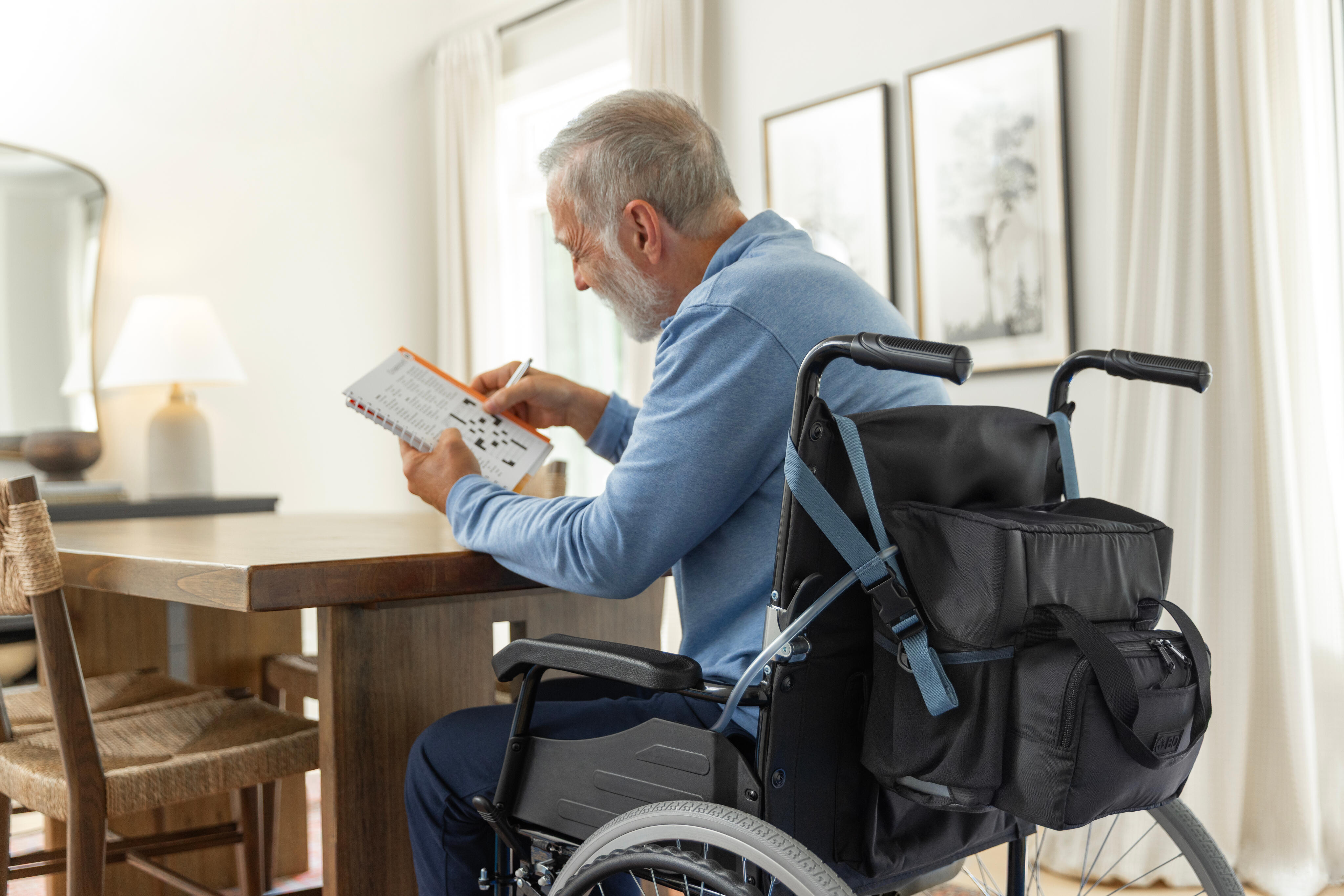 Man doing a crossword puzzle while sitting in wheelchair with PureWick&trade; Portable Collection System attached to back