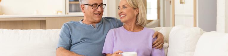 Man and woman on couch together smiling while she holds a coffee cup