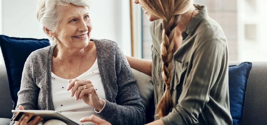 A woman sits on a couch with her daughter holding a tablet computer